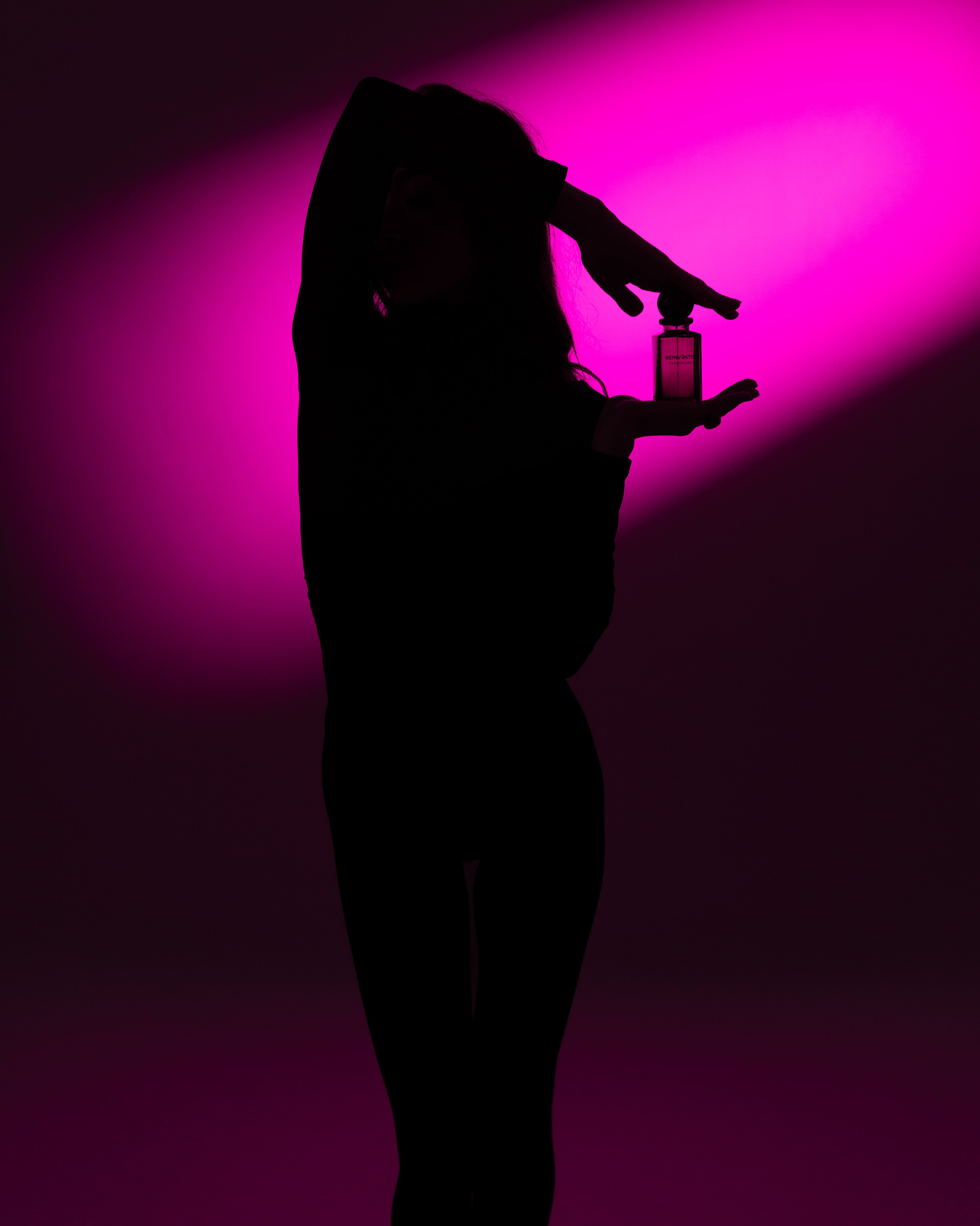 Image of Silhouette of a person holding a perfume bottle against a pink light