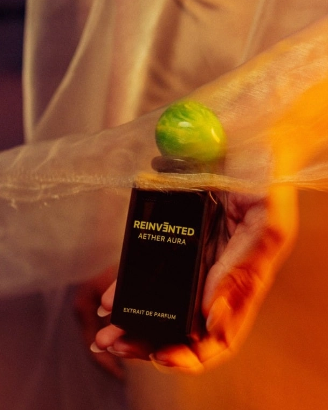 Image of Perfume bottle labeled 'Reinvented Aether Aura' held by a person with a blurred background
