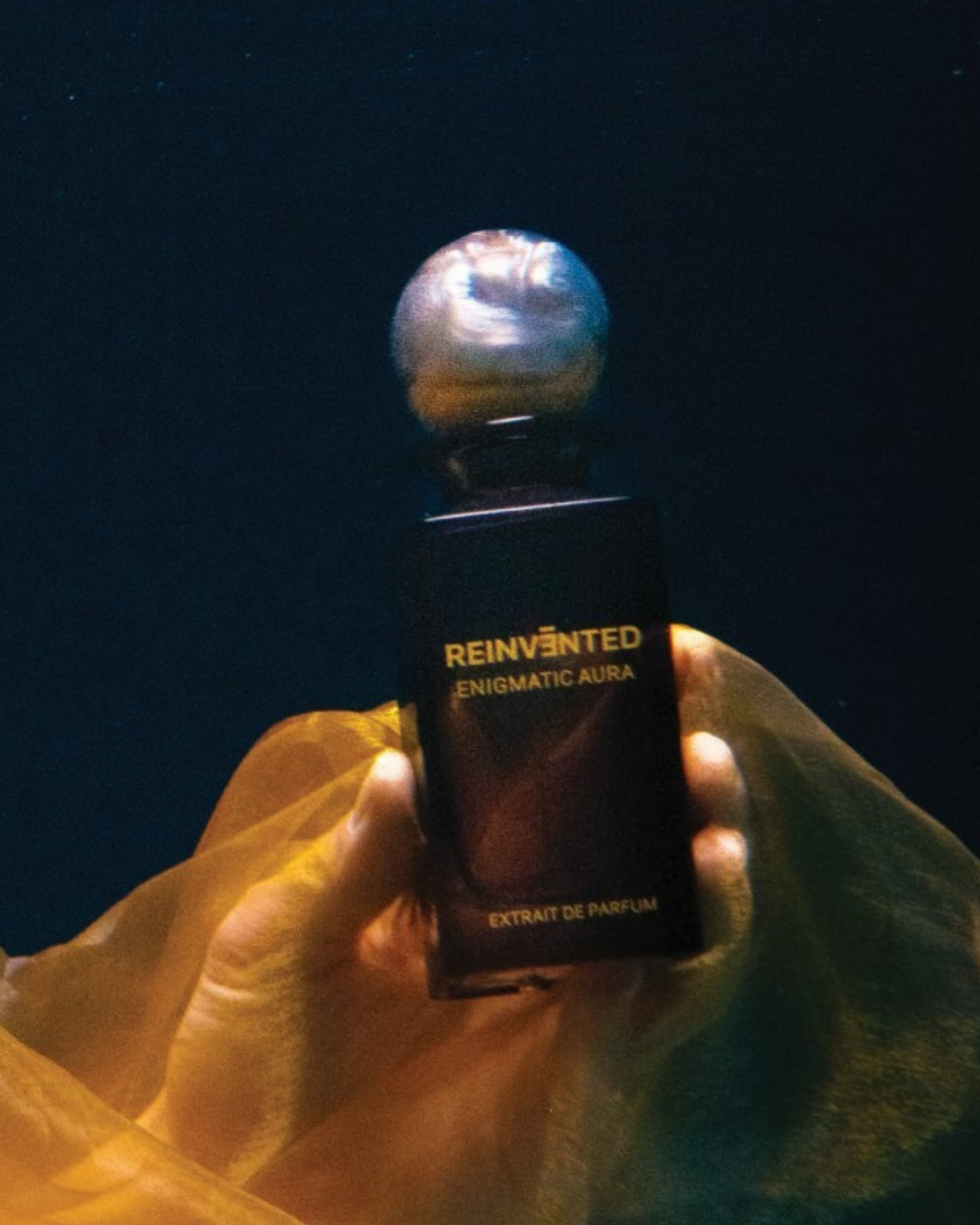 Image of Hand holding a perfume bottle labeled 'Reinvented Enigmatic Aura' against a dark background