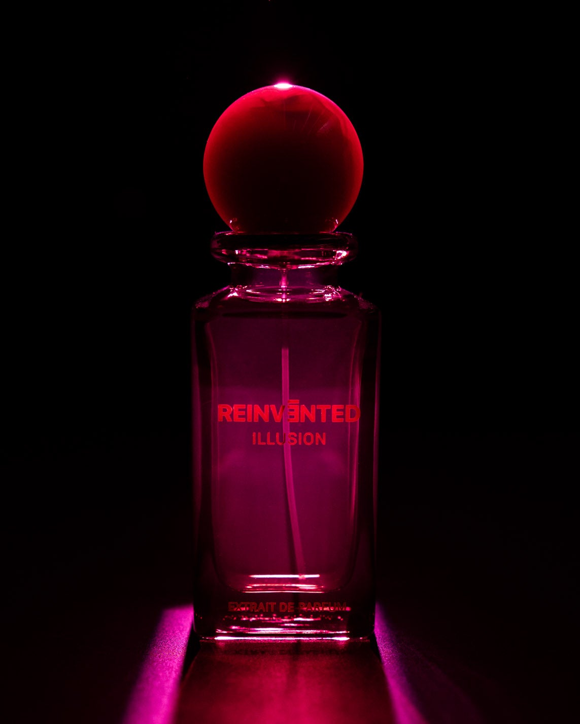 Image of Perfume bottle labeled 'Reinvented Illusion' with a red cap on a black background