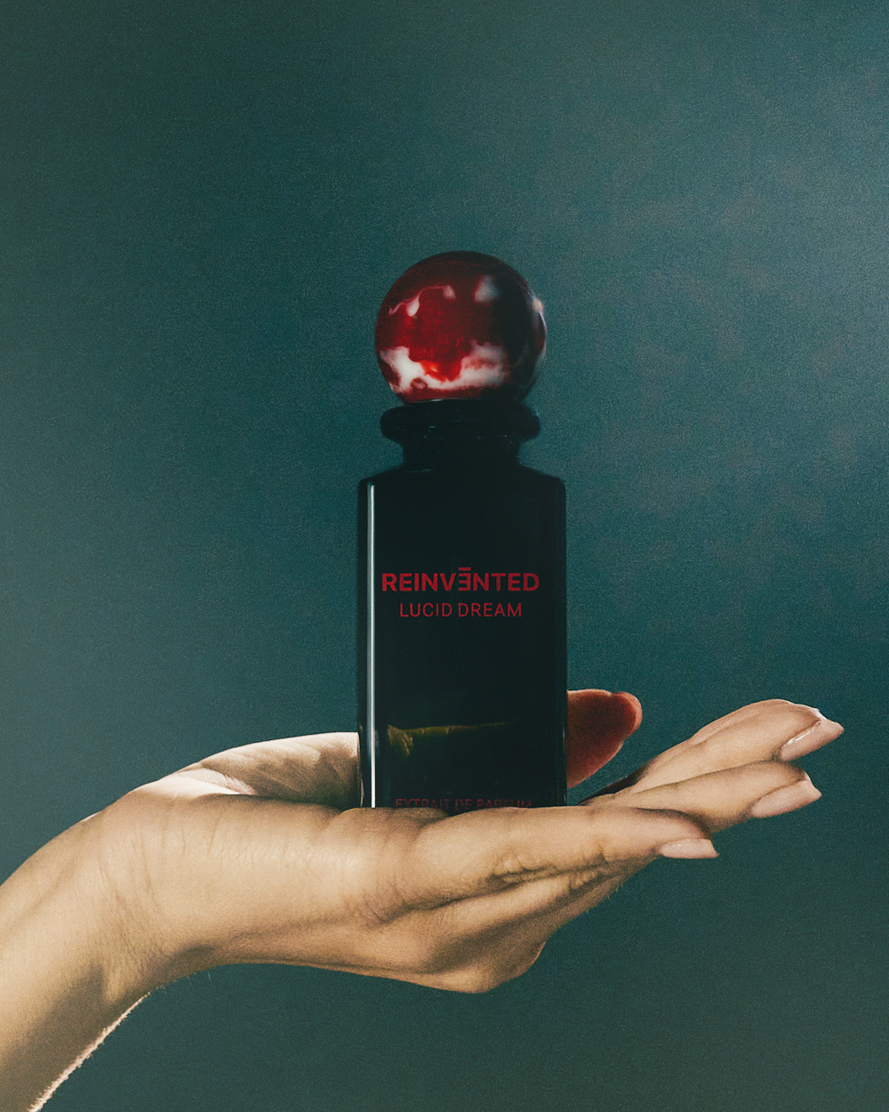 Image of Hand holding a black perfume bottle with red cap against a dark background