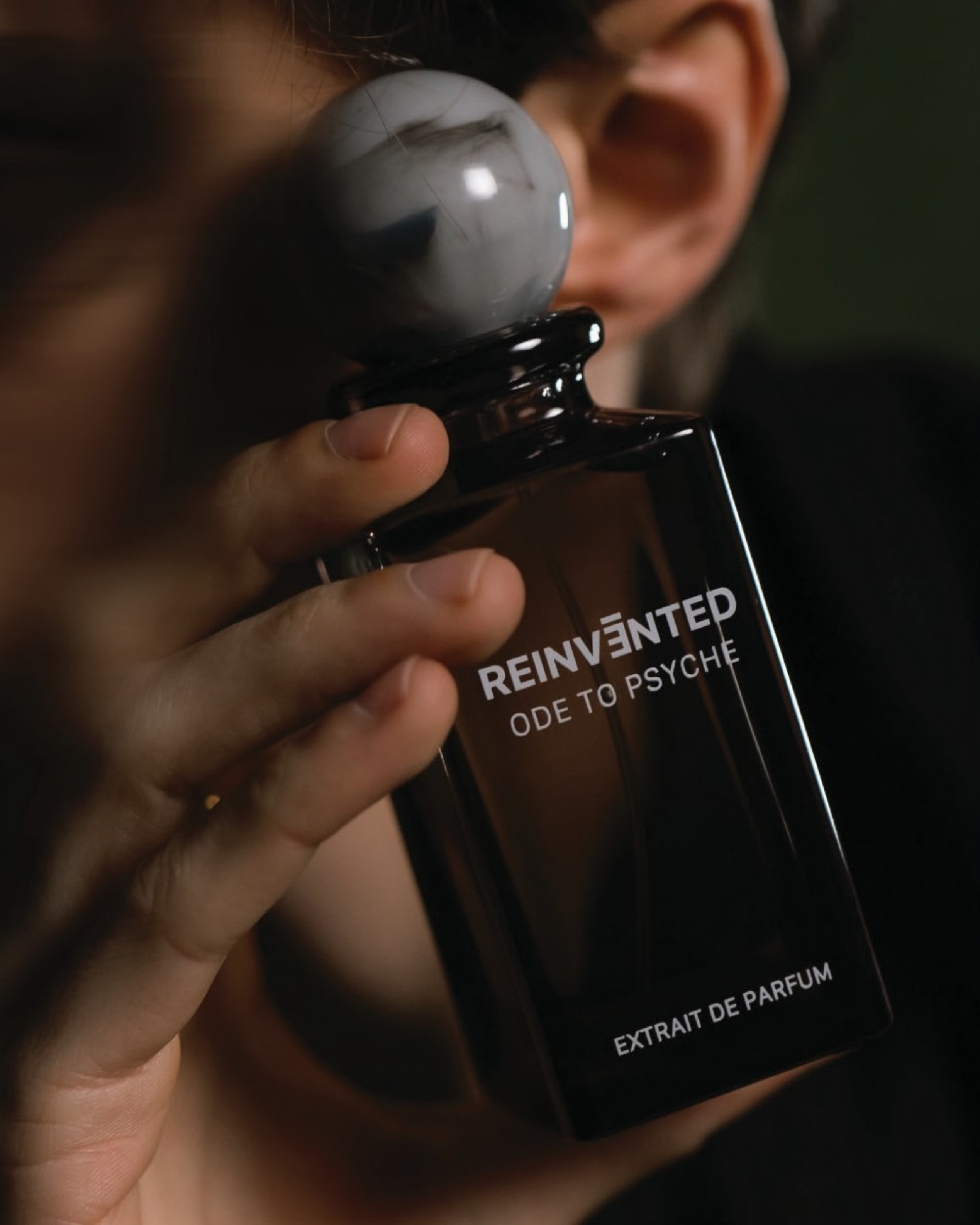 Image of Person holding a black perfume bottle labeled 'Reinvented Ode to Psyche' with a blurred background.