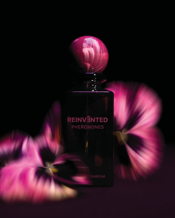 Perfume bottle labeled 'Reinvented Pheromones' with pink floral background