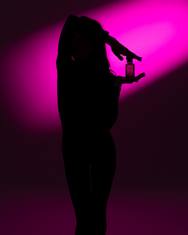 Silhouette of a person holding a perfume bottle against a pink light