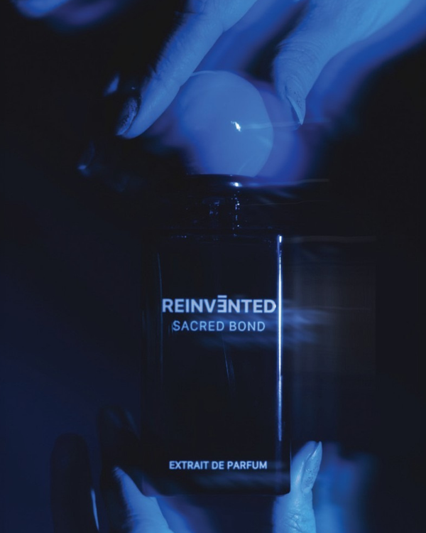 Black perfume bottle labeled 'Reinvented Sacred Bond' held by a hand in dark lighting.