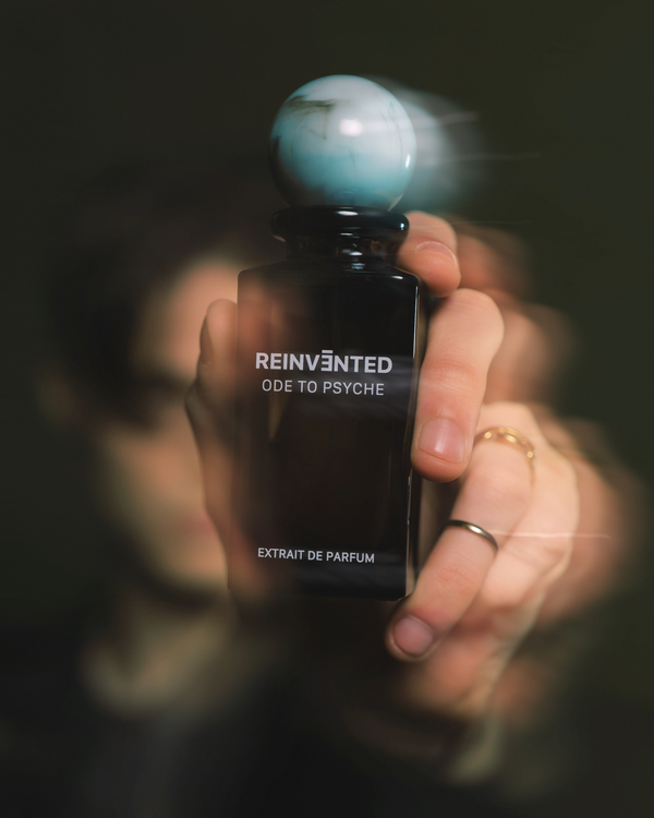 Perfume bottle labeled 'Reinvented Ode to Psyche' held by a hand with a dark background
